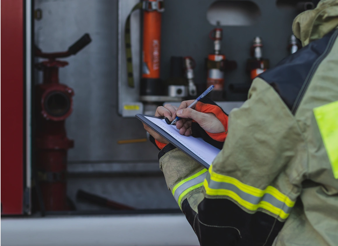 Firefighter writing notes on clipboard near equipment.