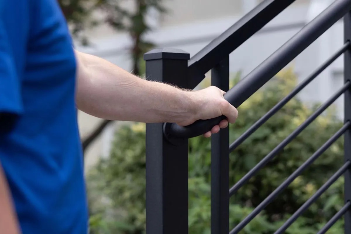 Hand gripping black metal outdoor stair railing
