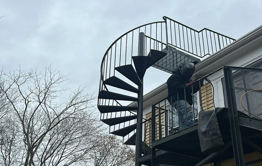 Person climbing outdoor spiral staircase, overcast sky.