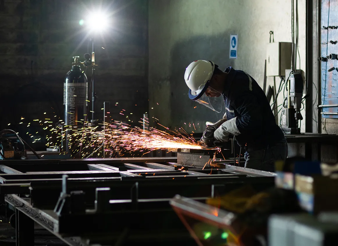 Worker grinding metal, sparks flying in workshop.