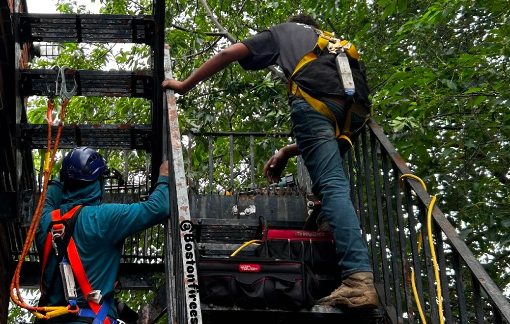 Workers climbing a ladder with safety gear.